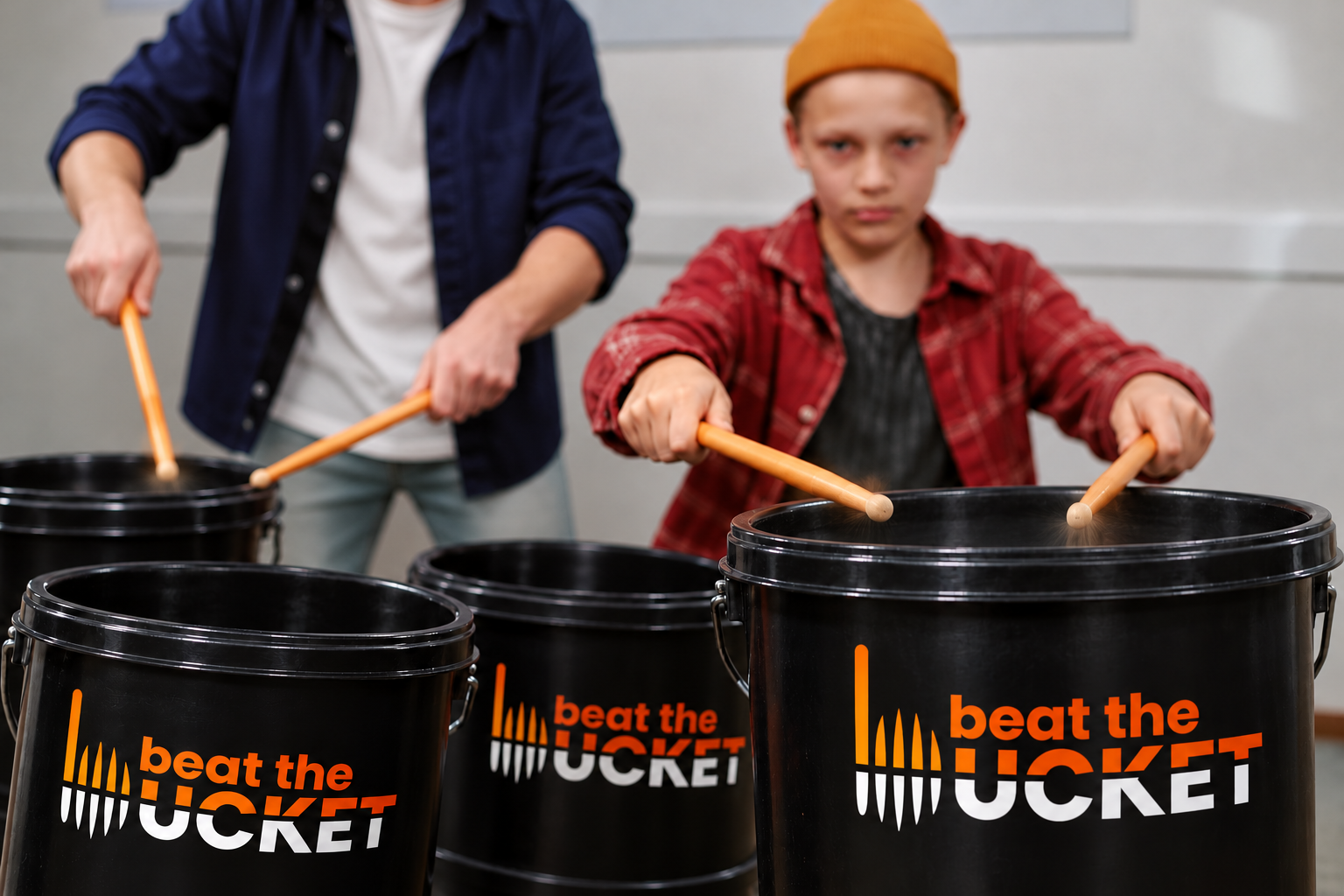 A young student and instructor using drumsticks on branded buckets in a school workshop.